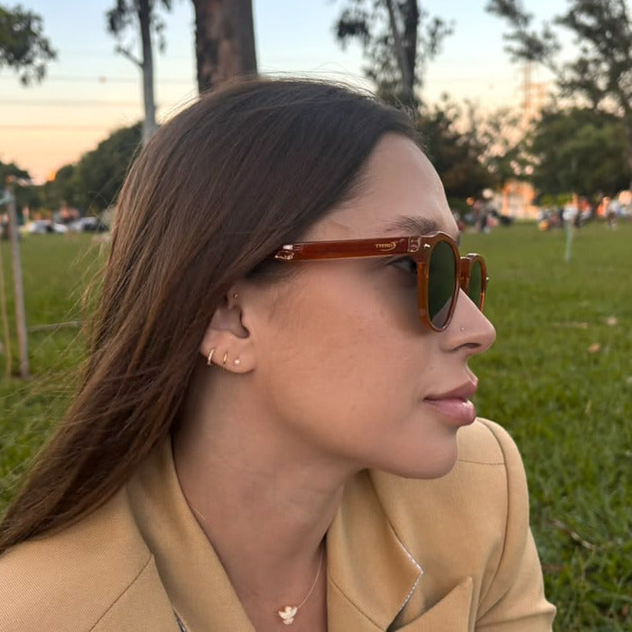 Model wearing Tyffco Mônaco sunglasses in Brown, side view showing the temple and the engraved mark, in a park at golden hour.